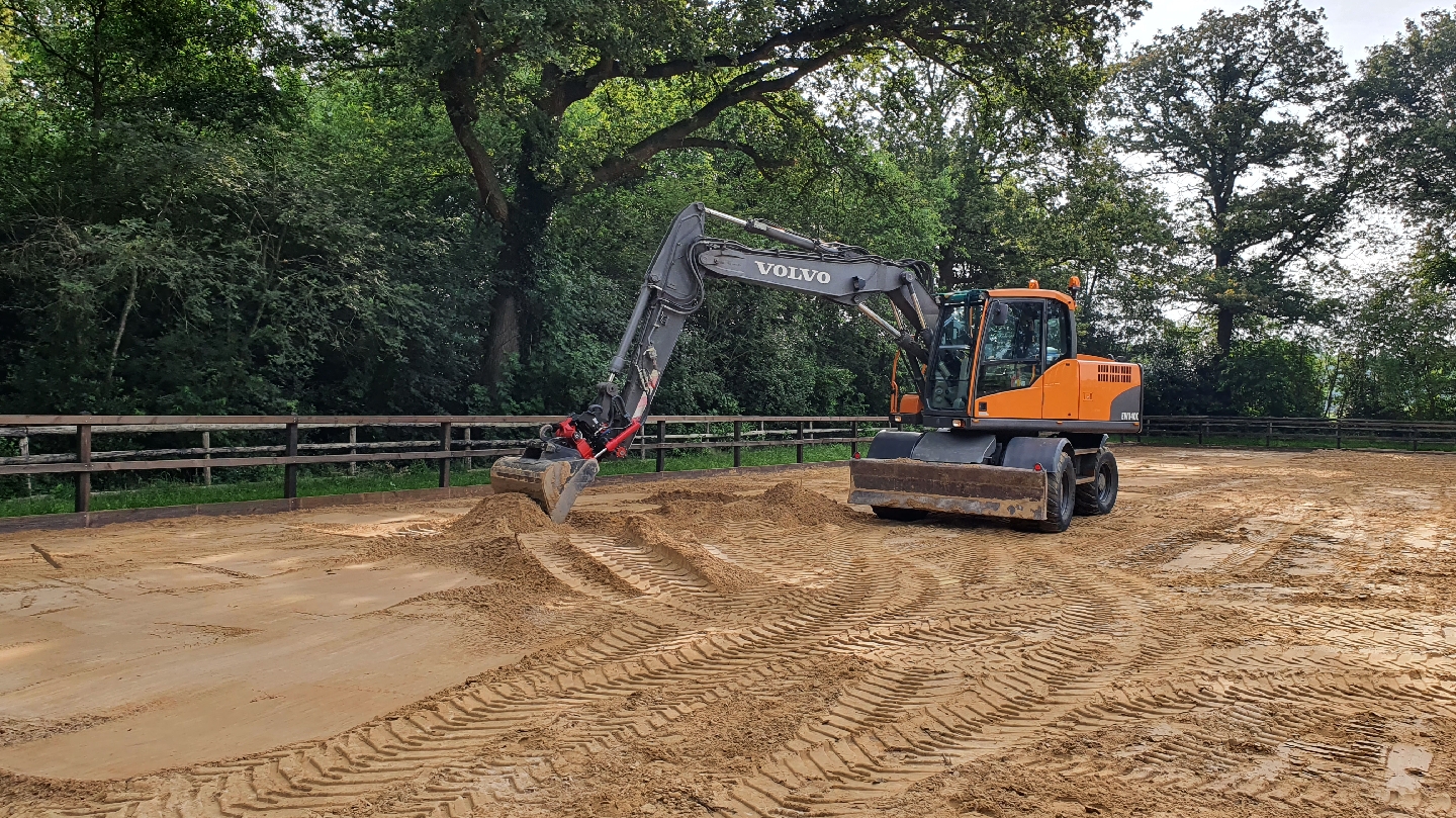 Volvo mobiele kraan egaliseert een zandbak, met een houten hek en bomen erachter