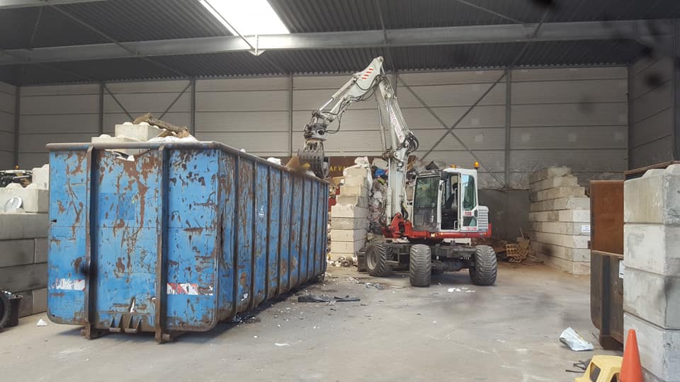 Kraan sorteert afval in een blauwe container in de hal