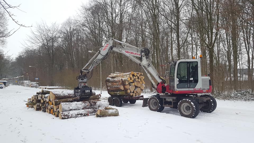 Kraan met grijper laadt boomstammen op een aanhanger in de sneeuw